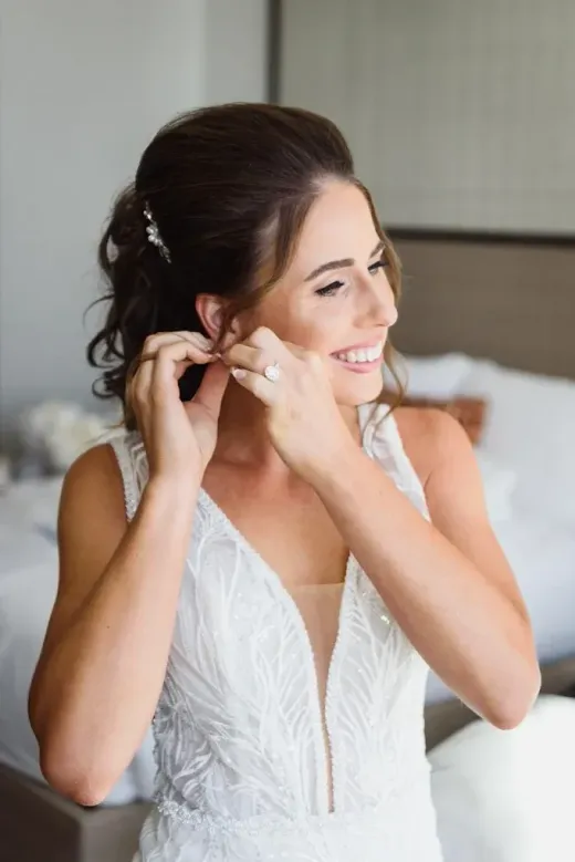Bride adjusting an earring in a lace gown, soft bridal glam