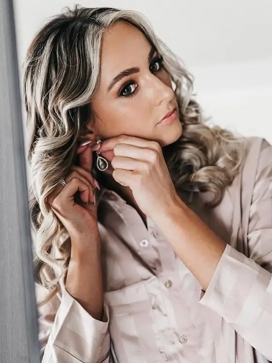 Bride fastening an earring in a satin robe, soft bridal glam